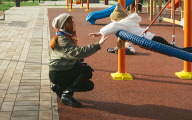 Mom and her daughter swinging on swing in autumn park. Happy family, child outdoors, weekend. Child girl, sits on swing smiles. Playground in fall.