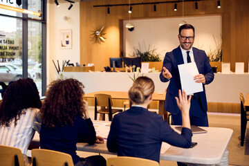 Professional Man In Suit Presents To Group In Modern Office During Business Meeting