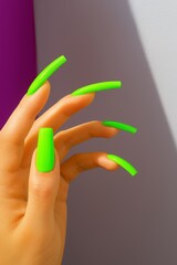 Close-up of a hand with long neon green acrylic nails against a neutral background, highlighting bold and vibrant manicure design.