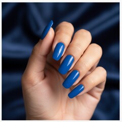 Close-up of a hand with long blue glossy acrylic nails against a satin blue background, showcasing bold manicure design.