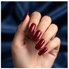 Close-up of a hand with long red acrylic nails resting against a smooth satin blue fabric, highlighting luxury and style.