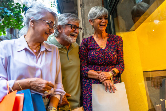 Senior friends enjoying window shopping with bags - Powered by Adobe