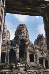 Naklejka premium Bayon temple's giant stone faces peer through an ornate window, showcasing khmer carvings and the spiritual, historic legacy of angkor thom in siem reap, cambodia