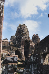 Fototapeta premium Ancient stone faces with serene expressions intricately carved on the tower of bayon temple, overlooking the rich archaeological complex of angkor thom in siem reap, cambodia