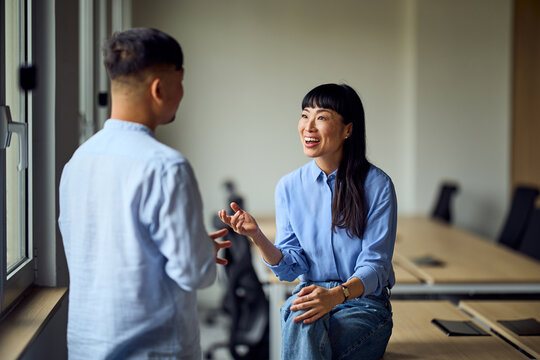 Asian Woman And Asian Man In Office Setting Discussing Ideas In Bright Workspace