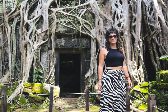 Young female traveler smiling beside ancient ta prohm temple, roots and jungle reclaiming mossy stone ruins in siem reap, cambodia  exploration, history and adventure combined