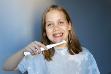 Girl smiles while brushing teeth in a well-lit room during morning routine