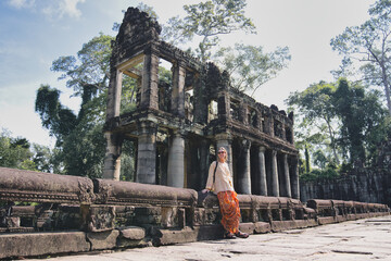 Woman standing beside ancient khmer temple ruins in cambodia, enjoying a cultural travel experience while visiting the historic preah khan archaeological site within the dense jungle