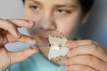 Young child holds dental retainer while smiling in bright room, showing improvement in oral health and alignment