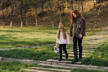 Mother and daughter walking on wooden path through autumn park. Warm clothes, plush toy, peaceful moment.