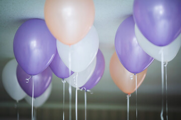 Obraz premium Colorful balloons in purple, peach, and white floating from the ceiling in a festive setting during a celebration or party