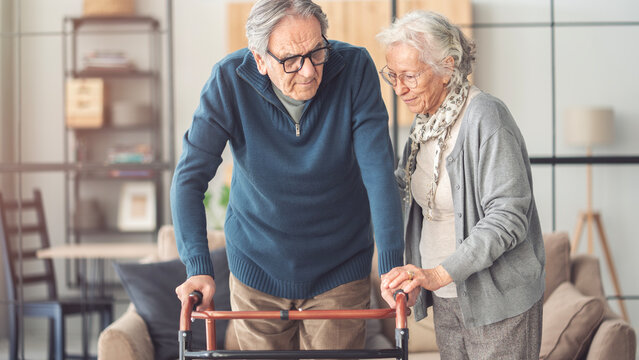 An elderly couple helps each other while using a walking frame