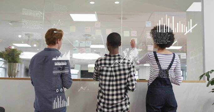 Planning team wearing casual attire placing post-its on glass board with digital graphs at office - Powered by Adobe