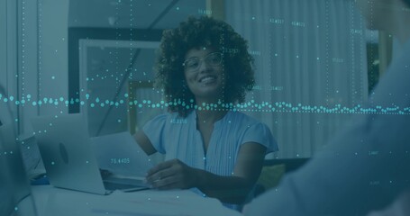 Holding papers, advisor with glasses in blue top meeting client in home office, laptop data overlay