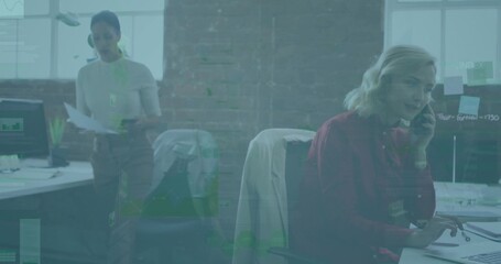 Speaking mid-adult woman wearing red blouse, using handset and typing at open-plan desk, copy space