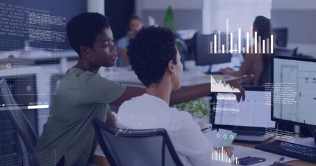 Pointing coworker in green top guiding colleague in white blouse at office, dual monitors overlays