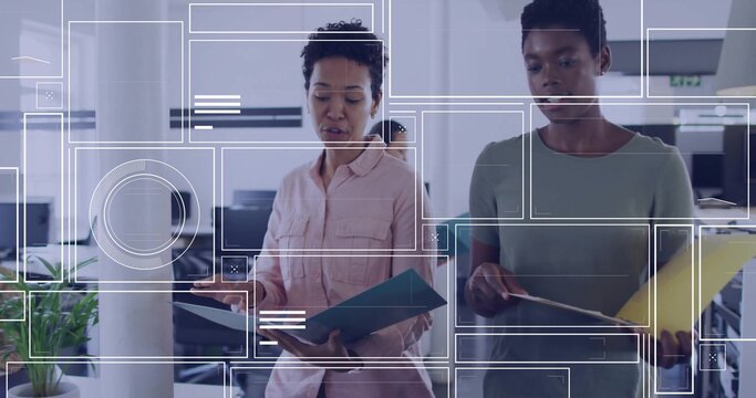 Reviewing paperwork, two coworkers in pink and green tops in office holding blue yellow folders - Powered by Adobe