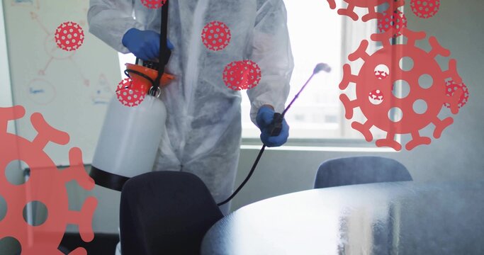 Spraying man in coverall blue gloves misting meeting room with handheld sprayer, red virus overlays