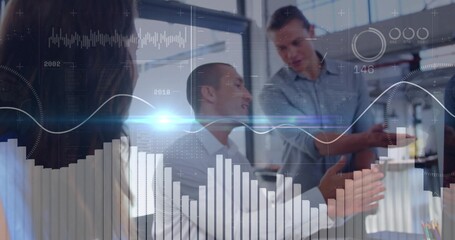 Gesturing man in dress shirt speaking with team in meeting area, with laptop and data charts