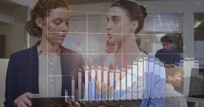 Analyzing two women in office attire examining financial charts on tablets with chart overlay