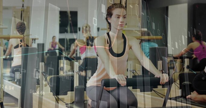 Sitting woman in tank, leggings holding bar at pilates studio with reformers, stock charts overlay