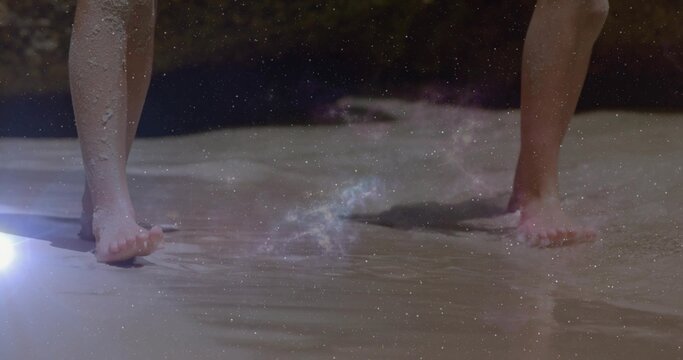 Wading two kids' bare feet in shallow shoreline water at beach, showing footprints and lens flare - Powered by Adobe