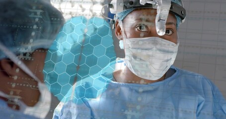 Operating surgeon with headlight, mask and blue gown performing surgery in OR, showing hex overlay