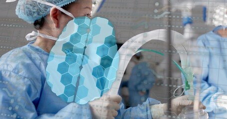 Operating surgeon in blue gown holding C-arm in OR with anesthesia mask, brain-overlay, copy space