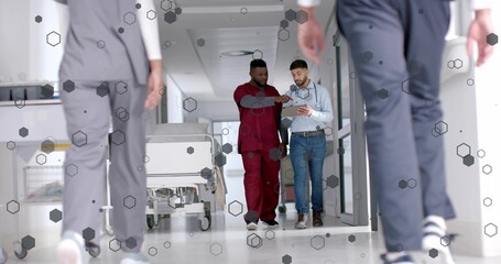 Walking men in scrubs and blue shirt with stethoscope examining tablet in hospital corridor gurney
