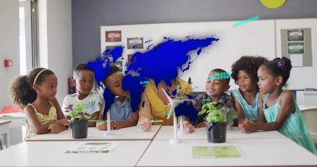 Leading teacher in yellow top leaning forward, handling turbine model at school table, with plants