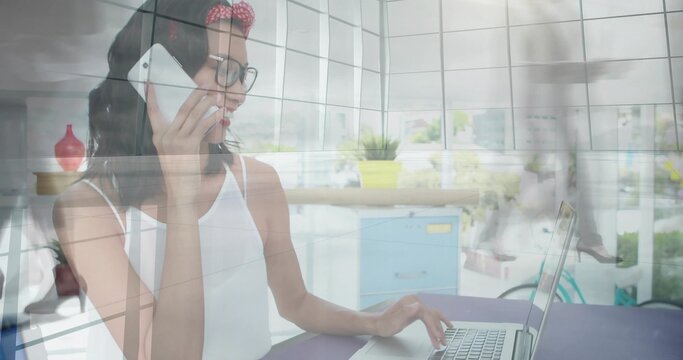 Talking woman in white top, glasses, red headband, holding phone reaching laptop in office