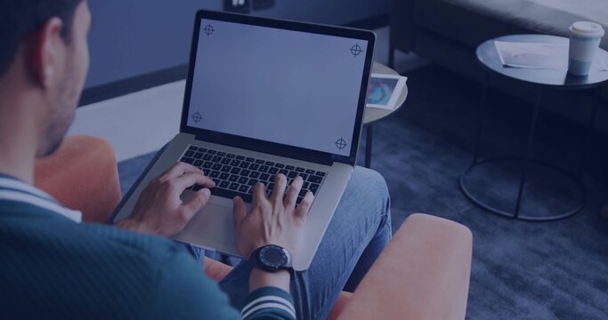 Typing man wearing green sweater on orange armchair in lounge, with laptop corner marks, copy space