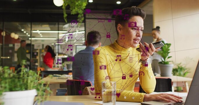 Speaking office worker in yellow turtleneck using laptop and phone in coworking space with plants - Powered by Adobe