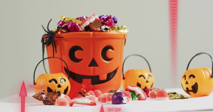 Showing orange pumpkin bucket spilling wrapped candies beside three pails on white table, spider