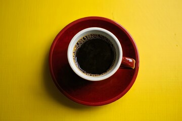 Single Cup of Black Coffee on Red Saucer Against Yellow Background