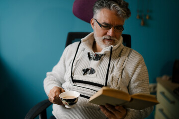 Older man enjoys a cup of tea while reading a book
