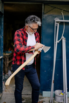 Man sharpening an axe while dressed in a plaid shirt at a workshop