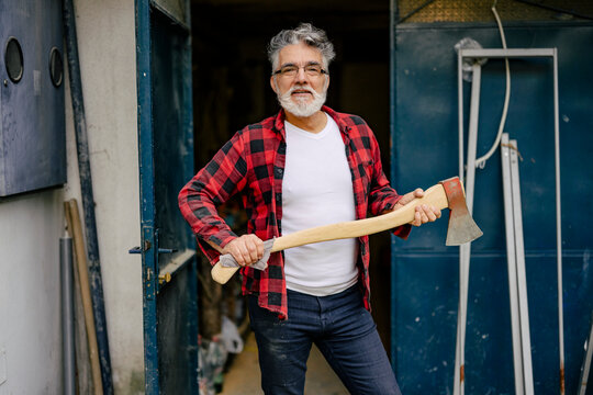 Man with an axe stands confidently in front of a workshop