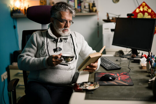Older man enjoys a cup of tea while reading a book
