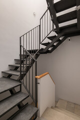 A modern staircase with metal railings and wooden accents. The stairs are gray and lead to an upper level in a minimalist interior design.