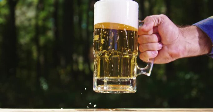Golden craft beer poured on green outdoors. Lager beer with foam in glass mug. Beer splash on nature background. Pouring amber ale in nature. Brewed beer with bubbles and foam. Craft brewery lager.