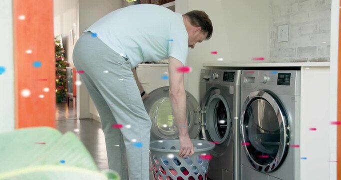 Mature man opening washer door loading clothes for laundry red or blue confetti floating around him