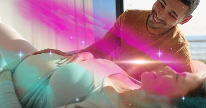 Man placing hand on pregnant woman's belly, sparking pink teal glow, couple bonding for health