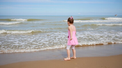 Little Girl in Pink Dress Walking Along the Beach as Gentle Waves Roll In.