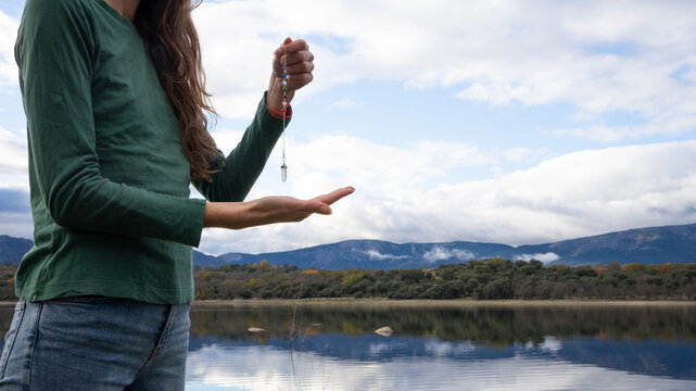 Woman holding crystal pendulum for spiritual dowsing outdoors