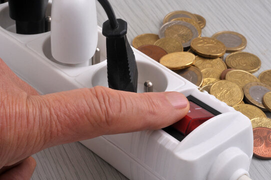 Concept d'économie d'énergie avec sur un doigt éteignant une multiprise, avec des pièces de monnaie en euros en arrière-plan