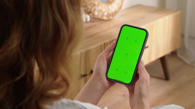 Woman sit use digital tech cell phone open green screen mock up. Hand scroll phone web site swipe unlock. Girl hold mobile closeup. Turn on chroma key page Cozy home background. Online app copy space