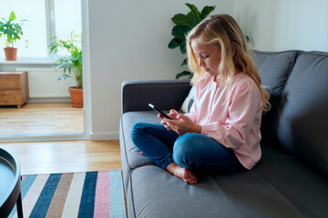 girl sitting on sofa using smartphone in modern living room, focusing on screen with serious expression, demonstrating technology use in medical care context