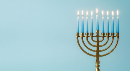 A brass menorah with nine lit blue-and-white candles set against a soft light-blue background,...