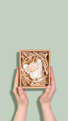 Christmas Angel Ornament Held In Gift Box On Green Background. Concept Of Winter Holiday Season, Handcrafted Presents, Christian Traditions, Festive Packaging, And Sentimental Wintertime Home Decor